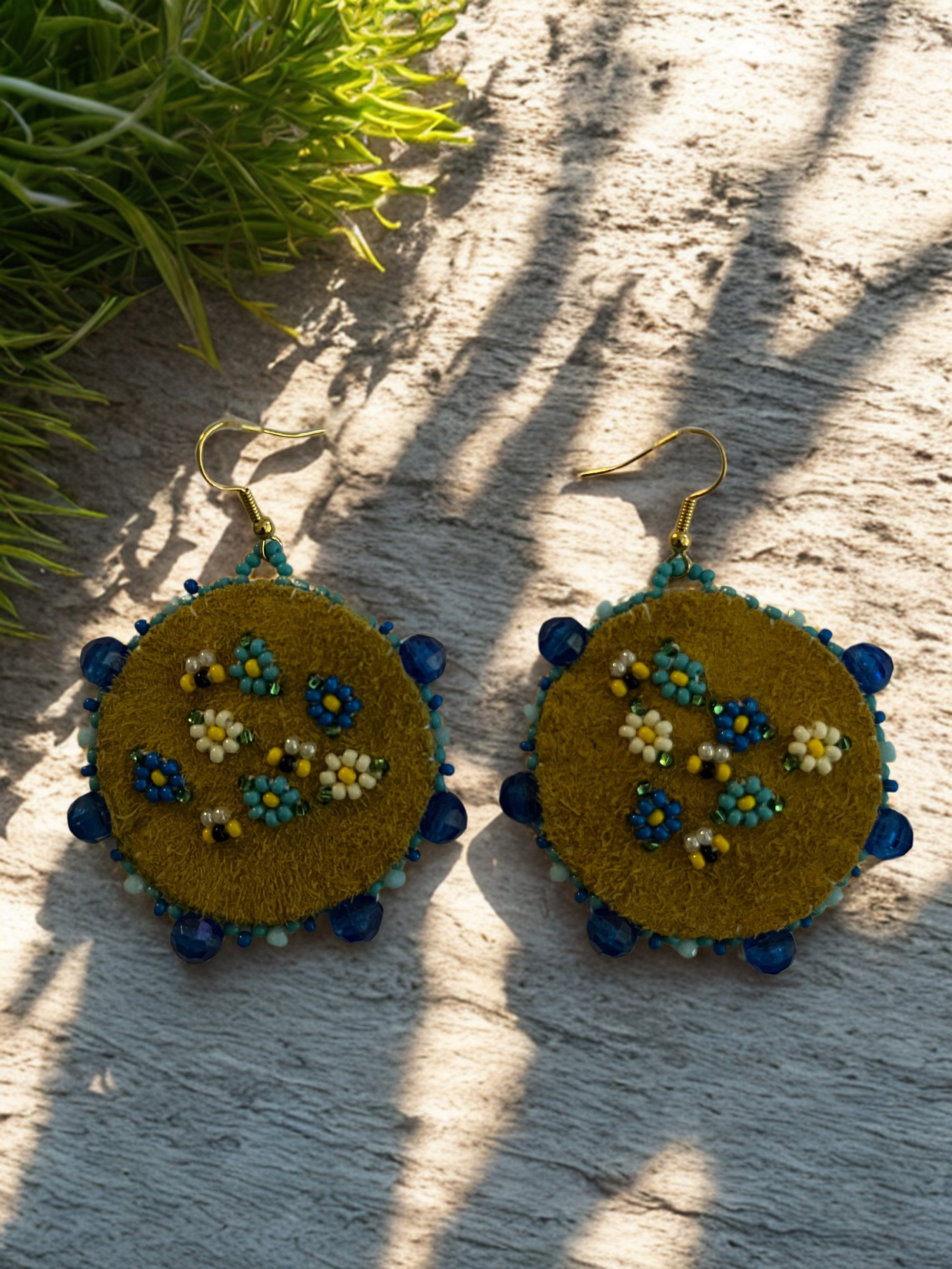 Pair of embroidered earrings on a textured surface with greenery in the background