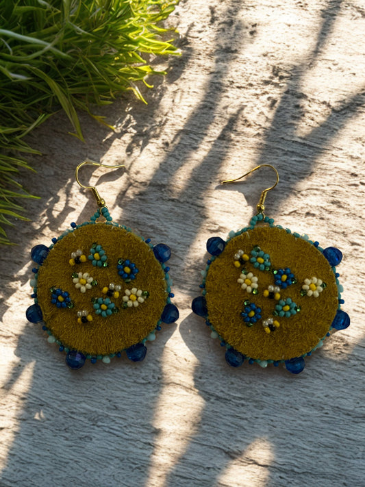 Pair of embroidered earrings on a textured surface with greenery in the background