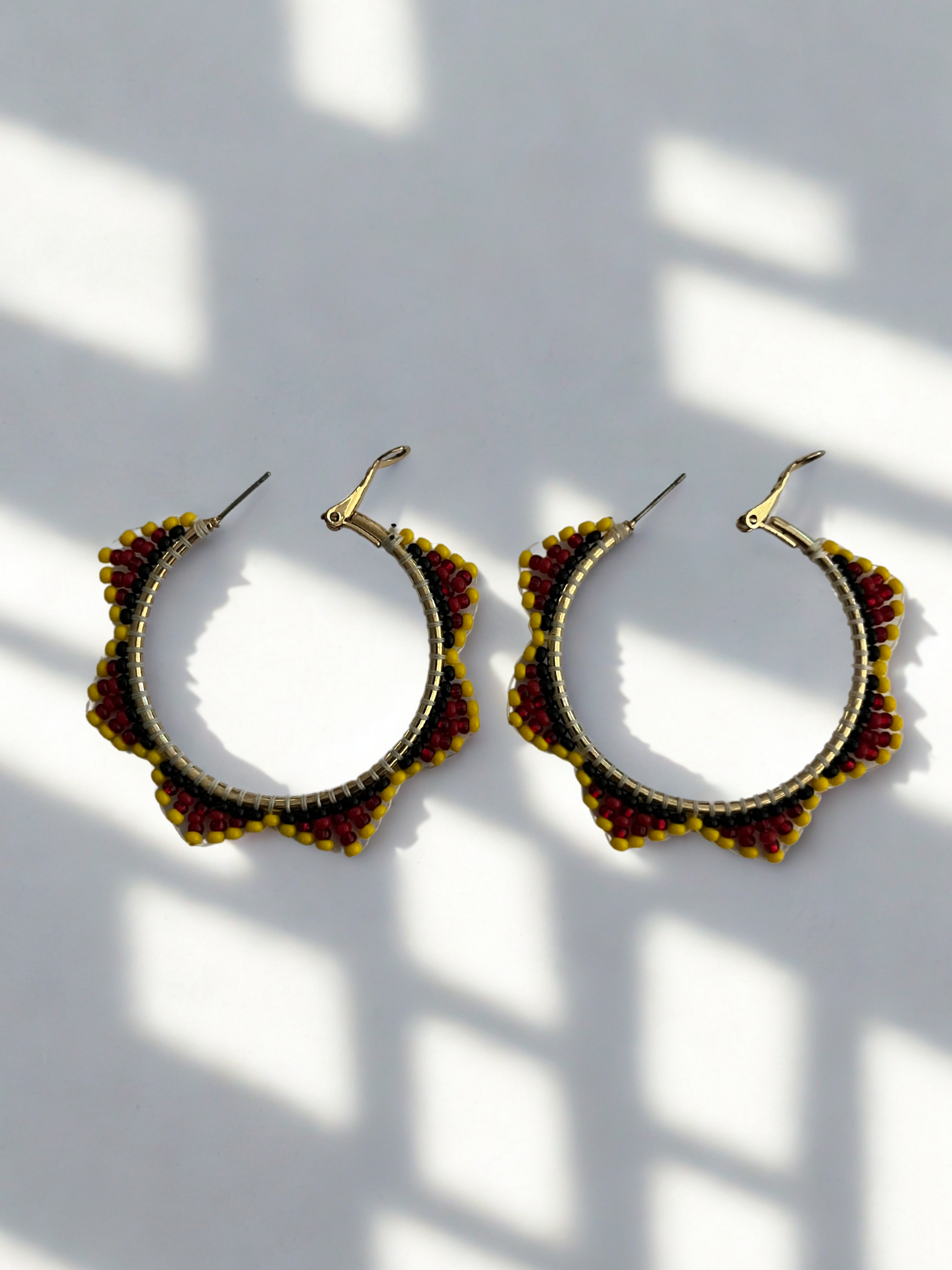 Pair of gold and red hoop earrings on a white background with shadows.
