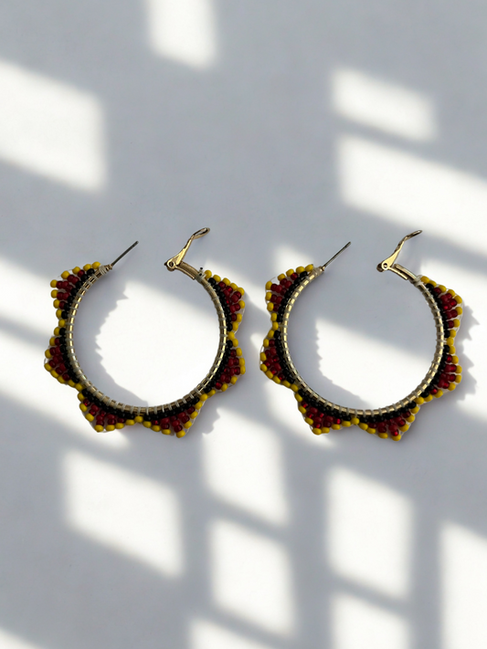 Pair of gold and red hoop earrings on a white background with shadows.