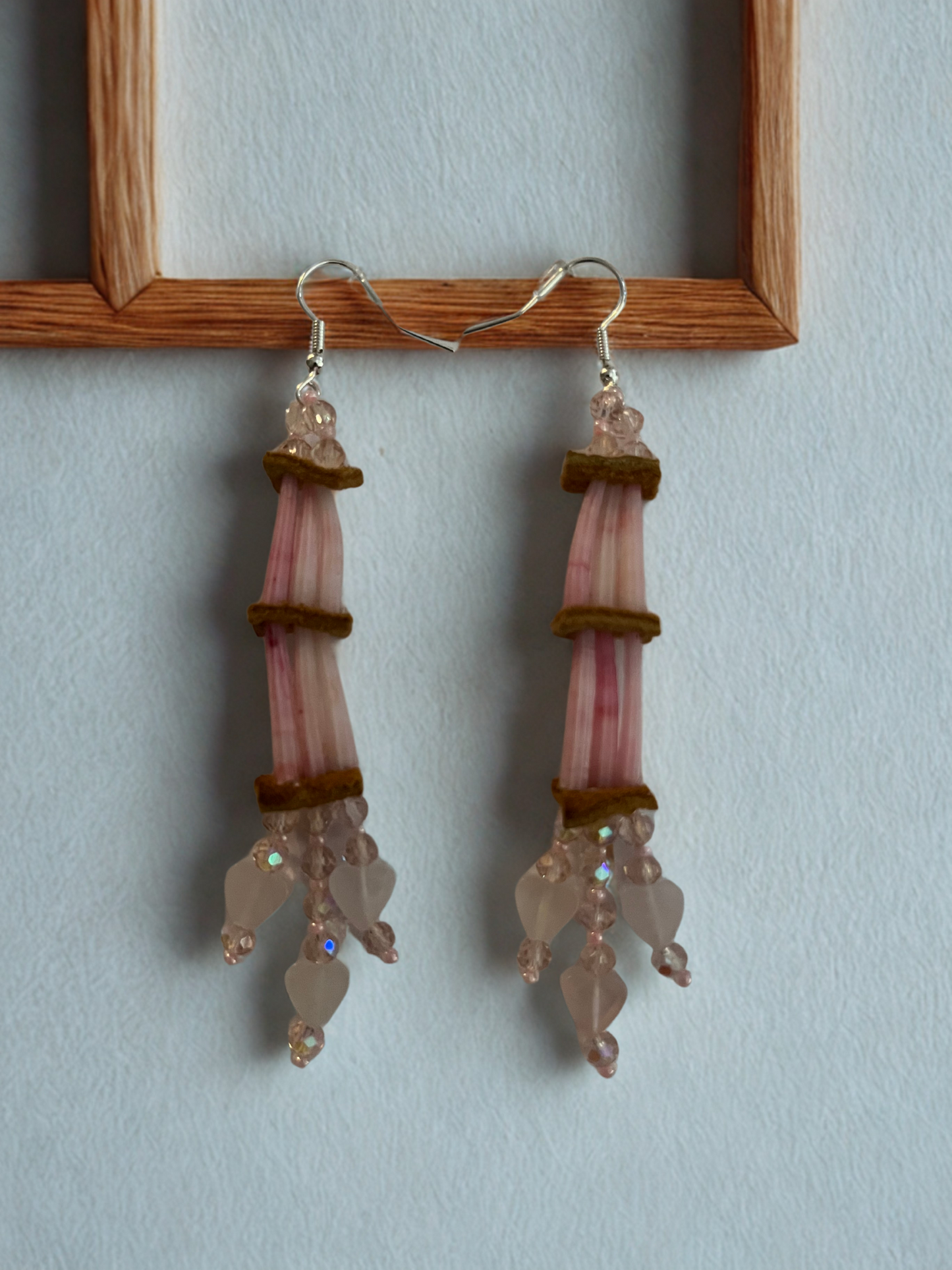 Pair of beaded earrings hanging on a light blue wall with a wooden frame.