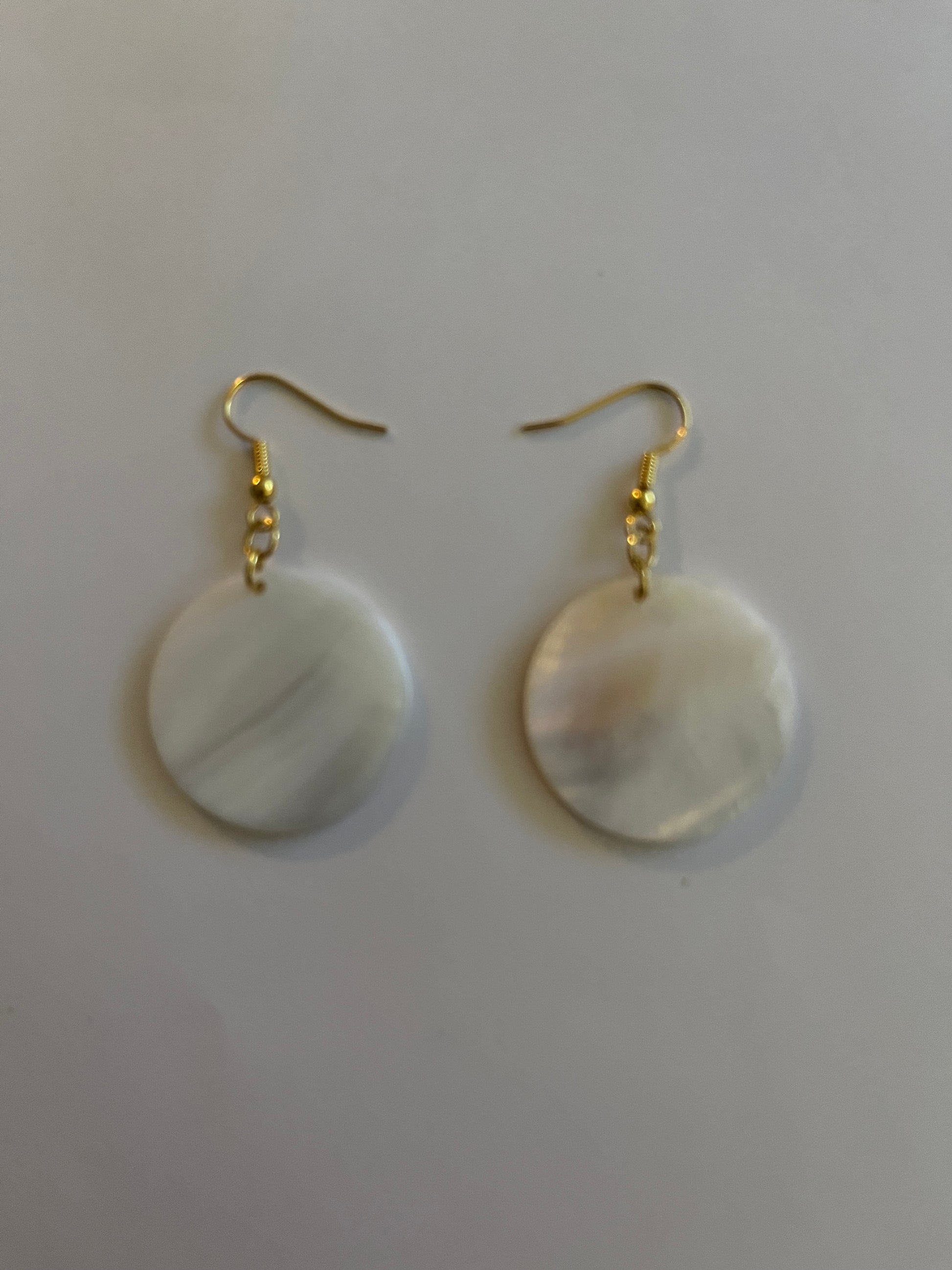 Pair of earrings with gold hooks and round, white stones on a light gray background