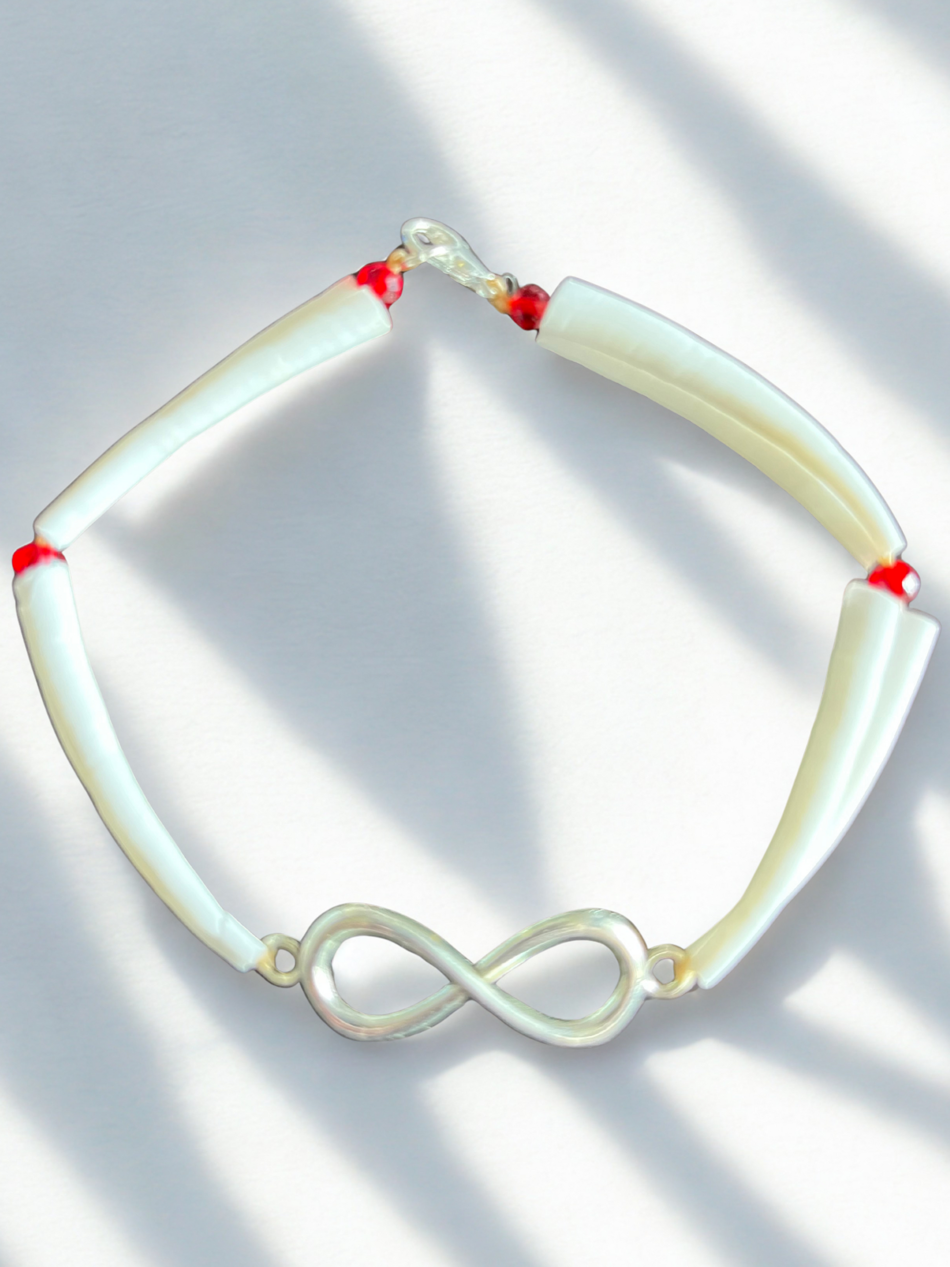 White dentalium shell bracelet with silver métis charm and red beads on a light background
