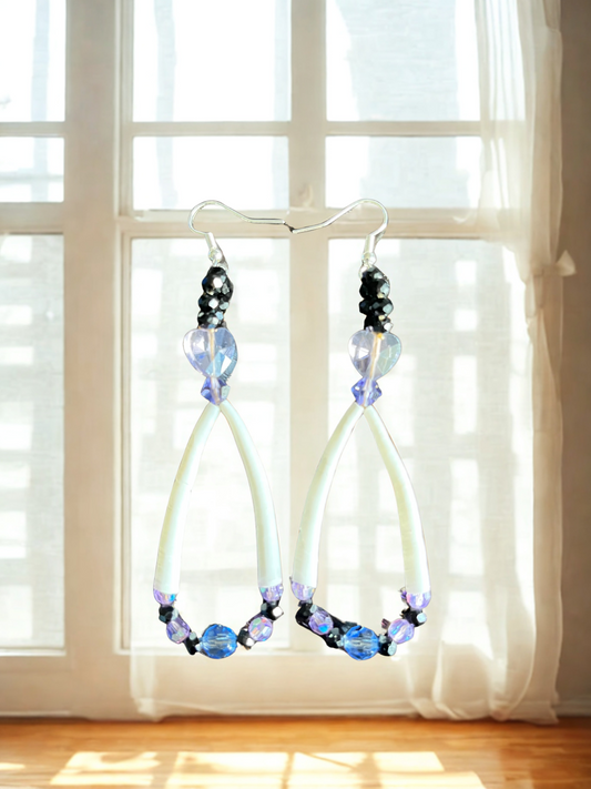 Pair of earrings with blue and purple beads hanging in front of a window.