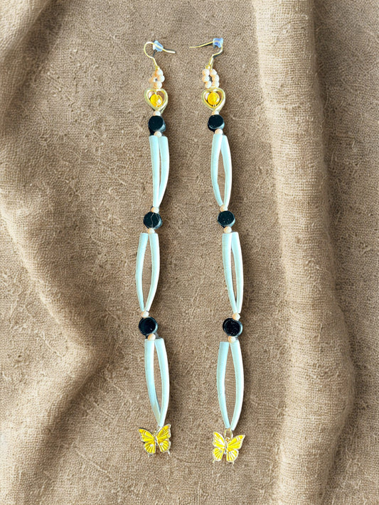 Long earrings with butterfly charms on a beige fabric background