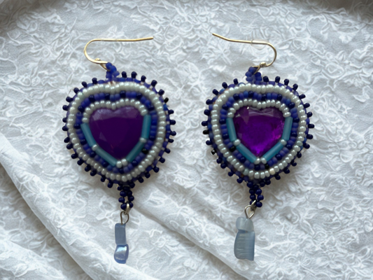 Heart-shaped beaded earrings with purple center on a textured white background