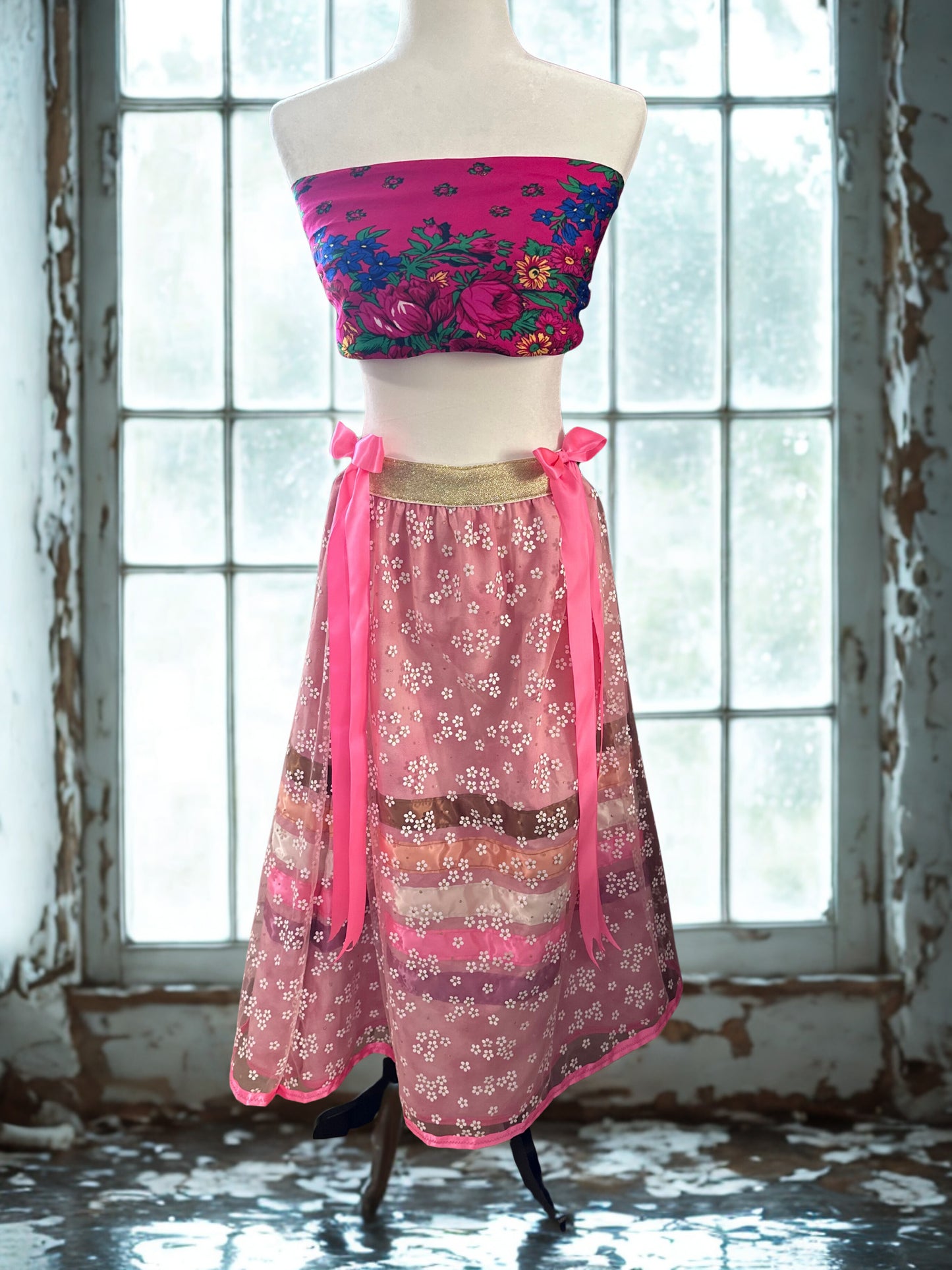 Mannequin wearing a colorful floral top and pink skirt in front of a window.
