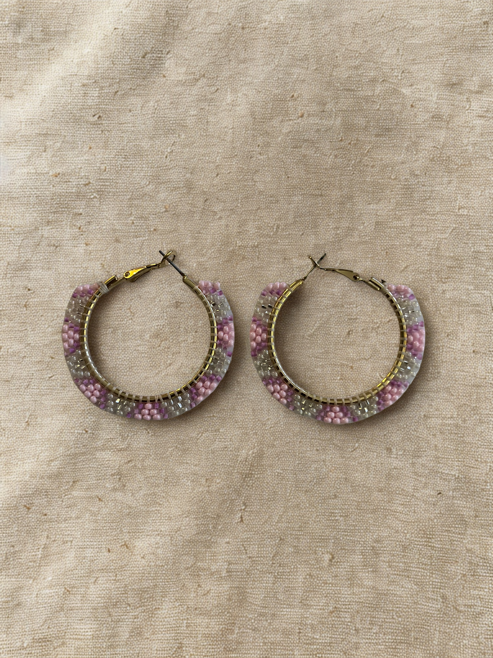 Hoop earrings with pink, white, and silver beads on a beige fabric background