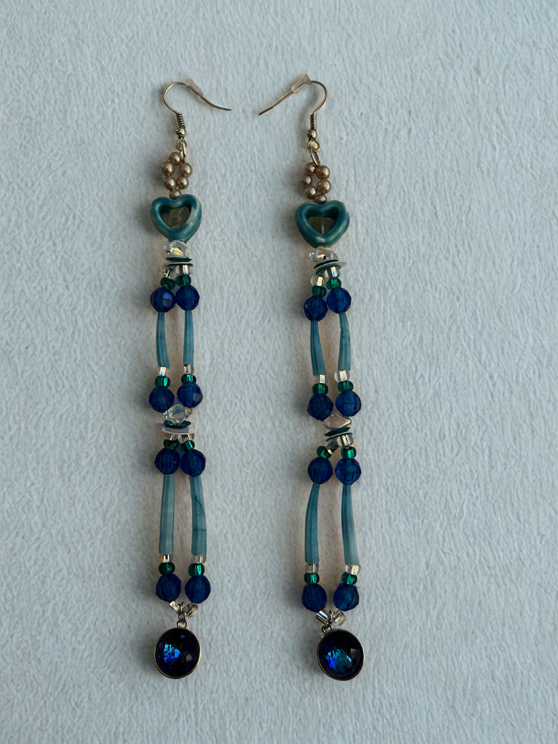 Pair of earrings with blue beads and heart-shaped charms on a light blue background