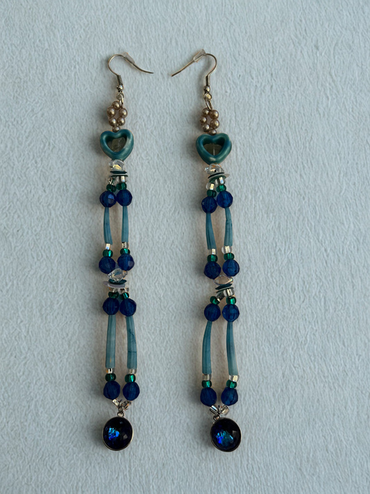 Pair of earrings with blue beads and heart-shaped charms on a light blue background